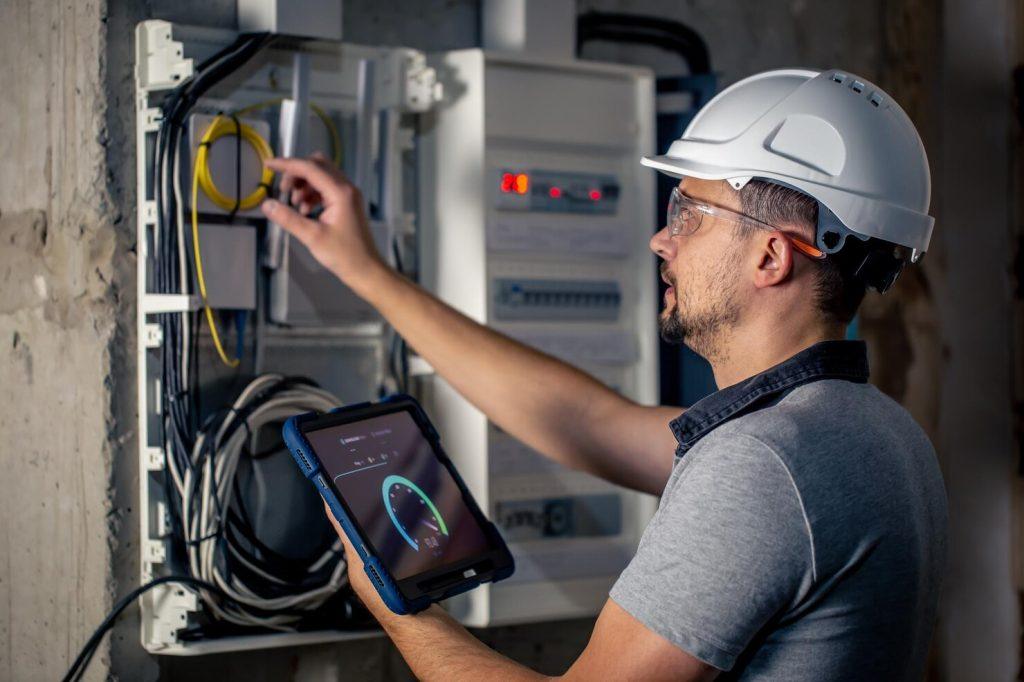 man electrical technician working switchboard with fuses uses tablet 169016 24219